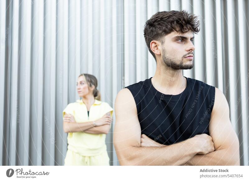 Thoughtful young couple standing in daylight against striped wall serious confident relationship arms crossed opposite calm disagree quarrel conflict gray