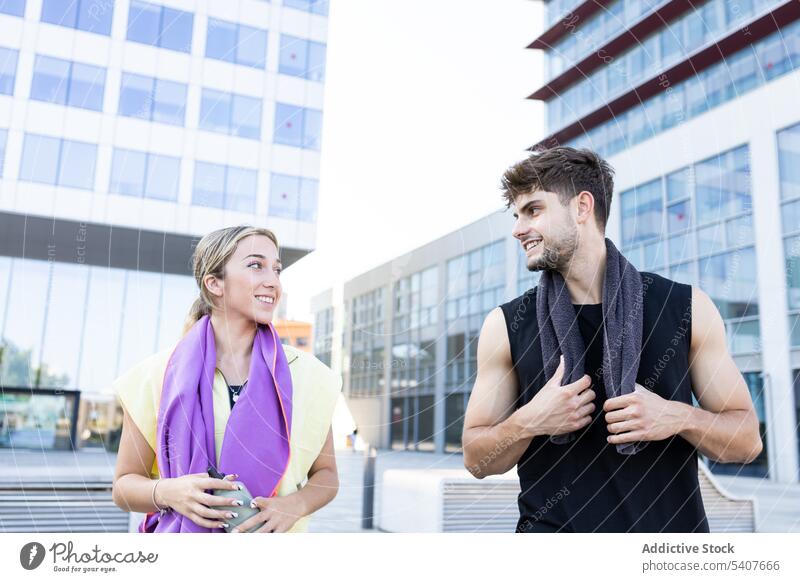 Happy young couple standing on city street in daylight near glass walled building towel bottle hydrate smile relationship love close positive happy athlete