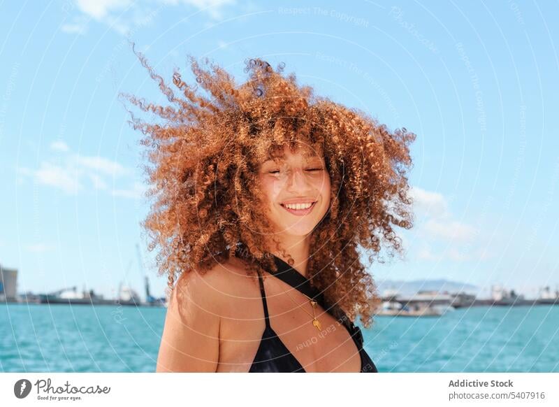 Carefree ethnic woman against blue sky enjoy summer sun carefree bikini top content relax afro female hairstyle vacation slim shorts cheerful sunny holiday
