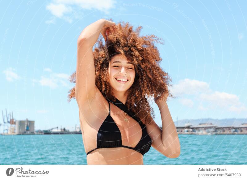 Carefree ethnic woman against blue sky enjoy summer sun carefree bikini top content relax afro female hairstyle vacation slim shorts cheerful sunny holiday
