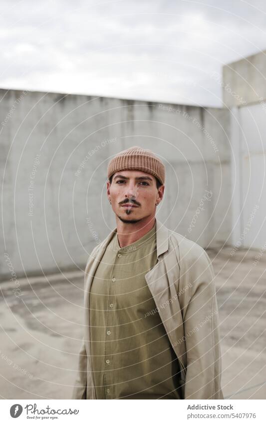 Stylish man standing in urban district in city style modern street coat trendy outfit appearance fashion male confident serious hat cool masculine emotionless