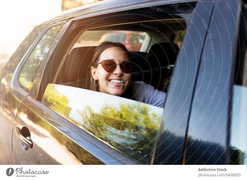 Delighted woman sitting in car and looking at camera backseat automobile cheerful relax modern parked city female positive young trendy joy smile rest optimist