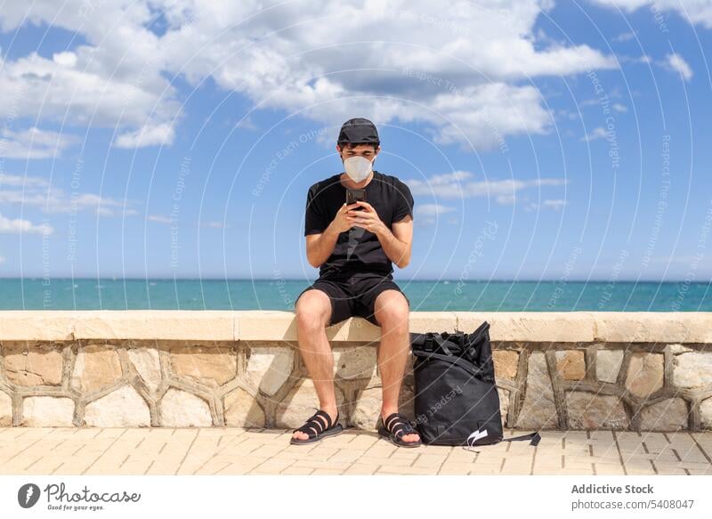 Man using smartphone near ocean man blue sky text embankment cloudy free time rest gadget mask covid 19 fence speak street device quarantine cellphone