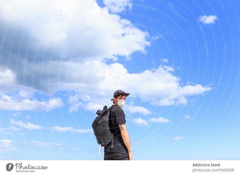 Male traveler standing under sky during summer trip tourist enjoy backpack dreamy freedom man nature blue sky cloudy mask covid 19 black apparel modern