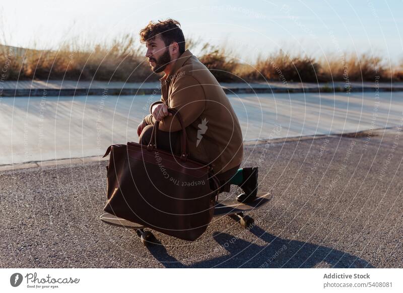 Young bearded skater with bag riding on road man longboard skill fashion style skateboard asphalt ride hobby activity male subculture countryside rural nature