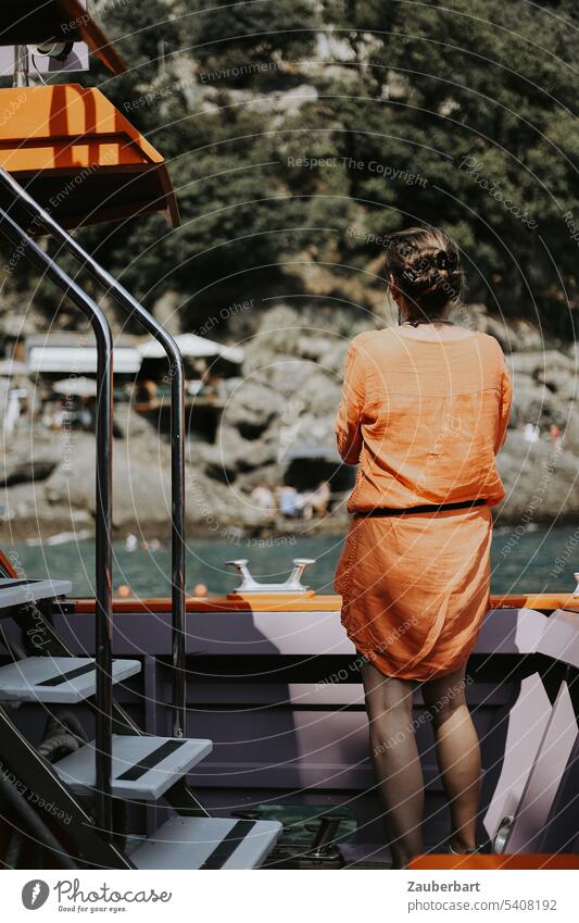 Tourist in orange dress stands on boat in bay on rocky coast on Italian Riviera tourist Orange Dress Italy Railing Observe travel sunny Water Ocean Summer