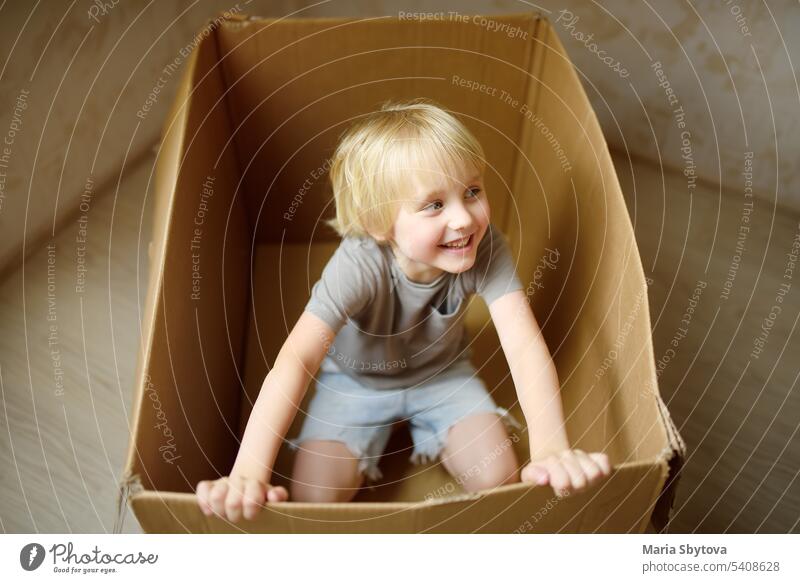 Cute preschool boy playing in a cardboard box during family's move to a new home. Kids play is a way of development of creative abilities. child carton inside