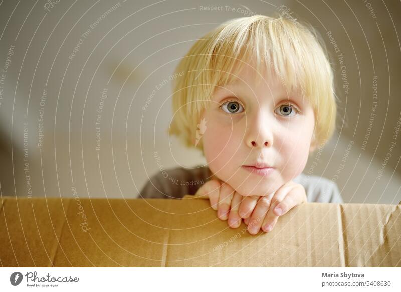 Cute preschool boy playing in a cardboard box during family's move to a new home. Kids play is a way of development of creative abilities. child kid children