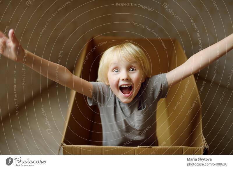 Cute preschool boy playing in a cardboard box during family's move to a new home. Kids play is a way of development of creative abilities. child kid imagination