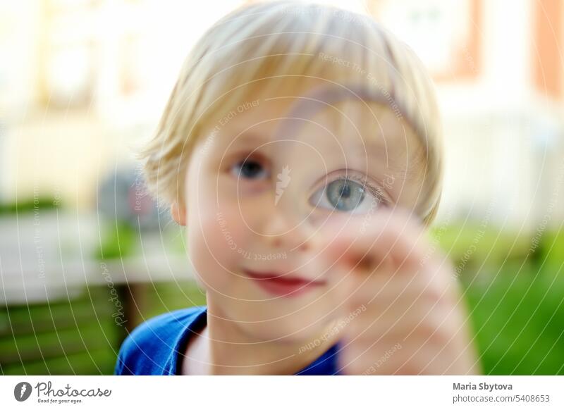 Little boy playing with magnifying glass. Baby carefully looking at you with magnifier. Activity for inquisitive child. Charming kid exploring nature with loupe.