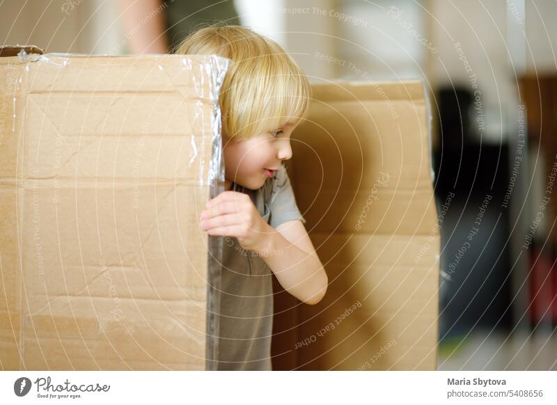 Cute preschool boy playing in a cardboard box during family's move to a new home. Kids play is a way of development of creative abilities. child carton inside