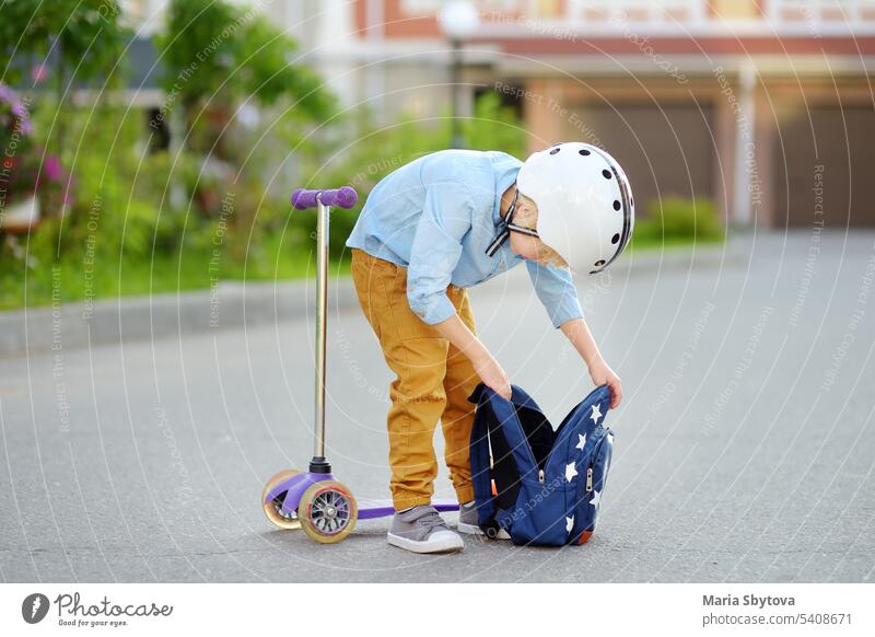 Little boy in safety helmet is riding scooter to school. Quality protect equipment for safety kids on street of city. Back to school concept. child schoolbag