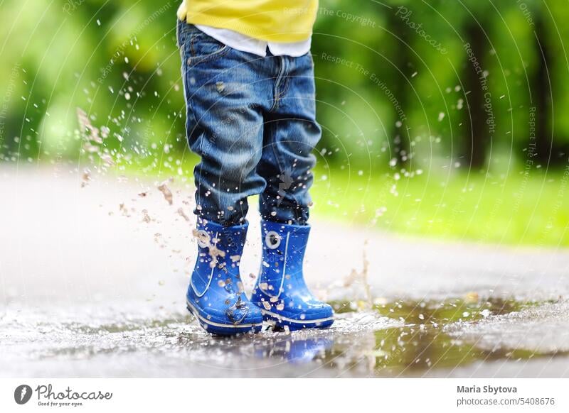 Toddler jumping in pool of water at the summer or autumn day. baby fun puddle outdoors child boy toddler rain boots playtime splash playful street park
