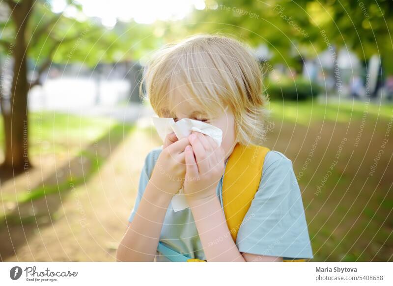 Preteen boy sneezing and wipes nose with napkin during walking in summer park. Flu season and cold rhinitis. Allergic kid. child allergic sneeze sick nature