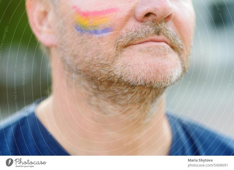 Close up view of face man activist with painting rainbow on cheek during LGBT Pride Event. Fighting for equality of rights of sexual minorities. lgbtq mature