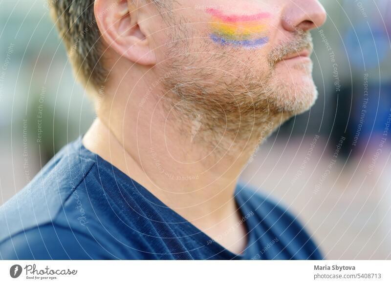 Close up view of face man activist with painting rainbow on cheek during LGBT Pride Event. Fighting for equality of rights of sexual minorities. lgbtq pride