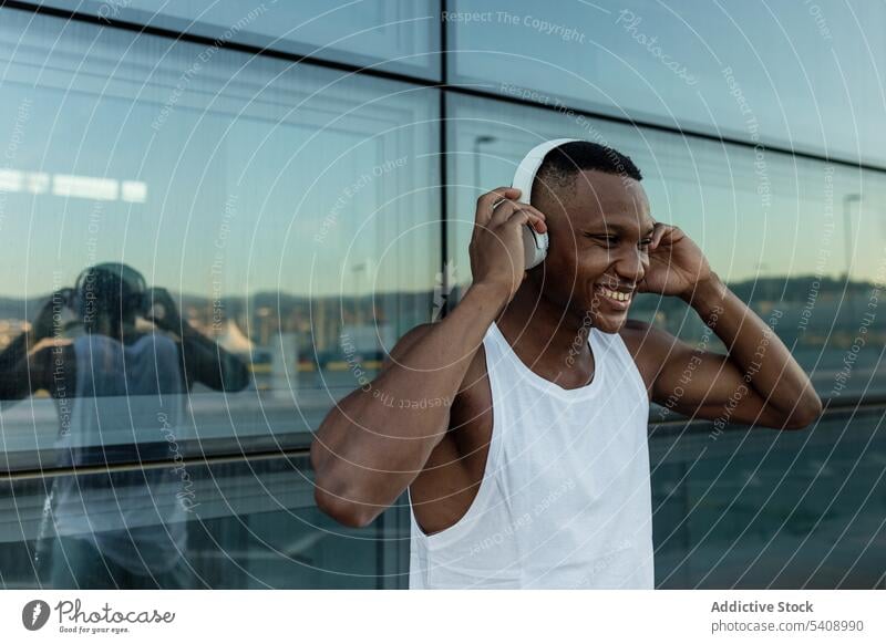 Cheerful black man listening to music in headphones cheerful joy sound athlete wireless optimist male training device gadget smile melody song guy tune rest