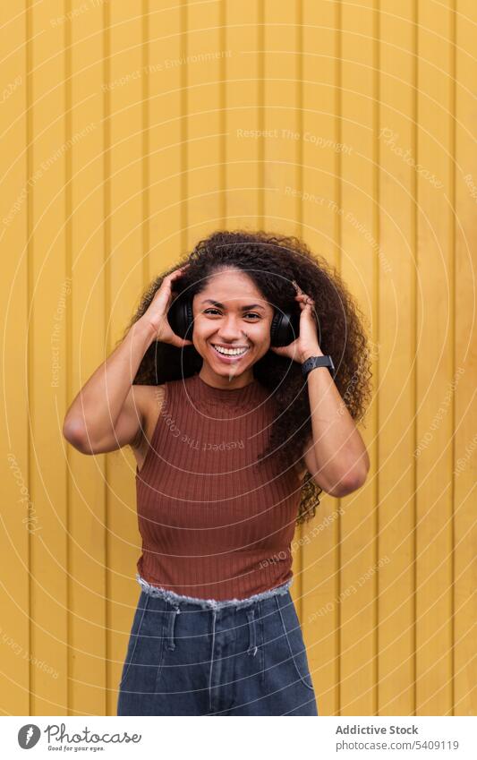 Charming ethnic woman with headphones on street curly hair afro hairstyle charming smile natural beauty female listen black african american city trendy rest
