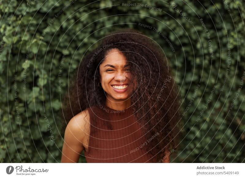 Happy ethnic woman in green garden charming smile natural beauty candid curly hair afro hairstyle park female black african american young happy cheerful joy