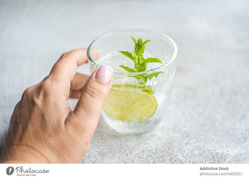 Crop person with glass of lime lemonade drink refreshment mint cold beverage hand soda tasty vitamin delicious fruit citrus sour slice leaf flavor tropical cool