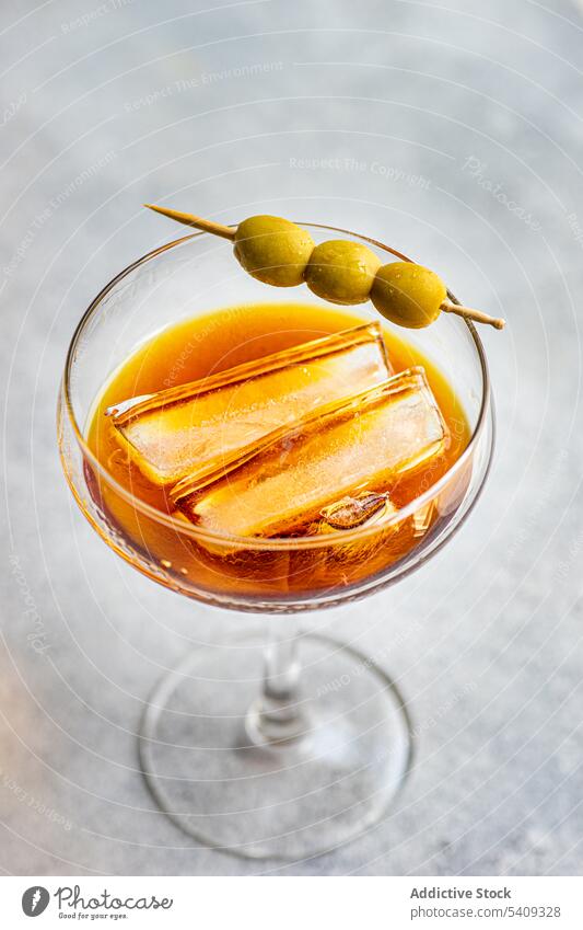 Glass of cocktail with whiskey alcoholic drink and sticks of olives ice glass glassware slice portion aperitif serve beverage yummy delectable tasty ingredient