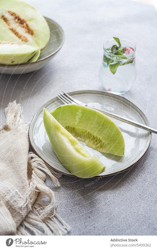 Honeydew green variety of melon fruit for dessert still life background pieces immature big drink white ceramic plate light colored glass table dish fresh