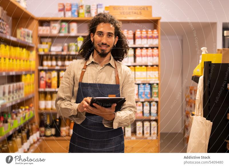 Delighted man with tablet checking goods in grocery store shop supermarket inventory control smile food gadget curly hair focus shelf happy cheerful delight