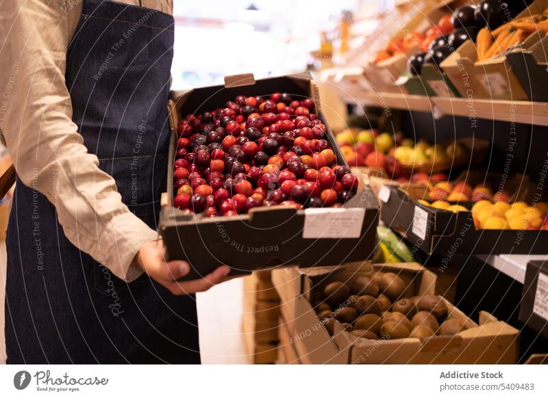 Anonymous male seller showing box of rope plums in supermarket man fruit grocery vegetable demonstrate ripe healthy food counter young african american ethnic