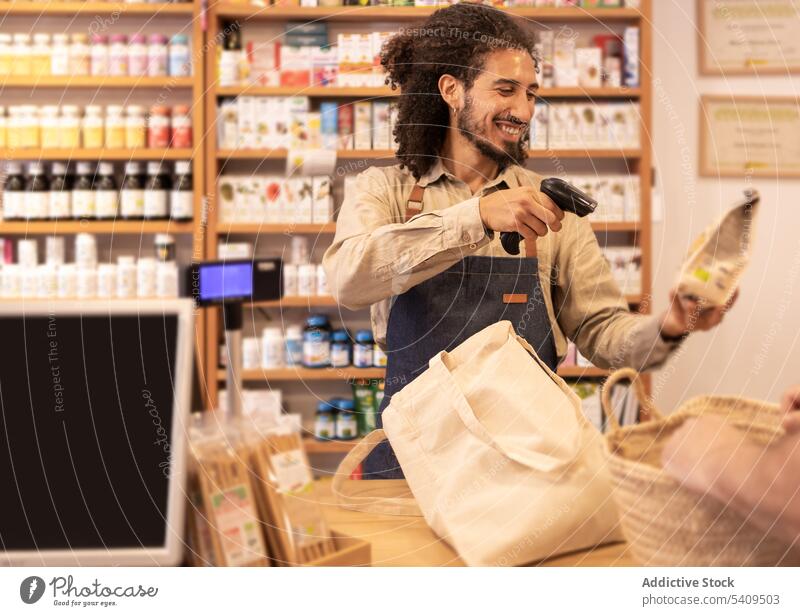 Smiling ethnic male seller scanning products at cashier counter man smile eco friendly cheerful grocery customer happy small business owner young hispanic