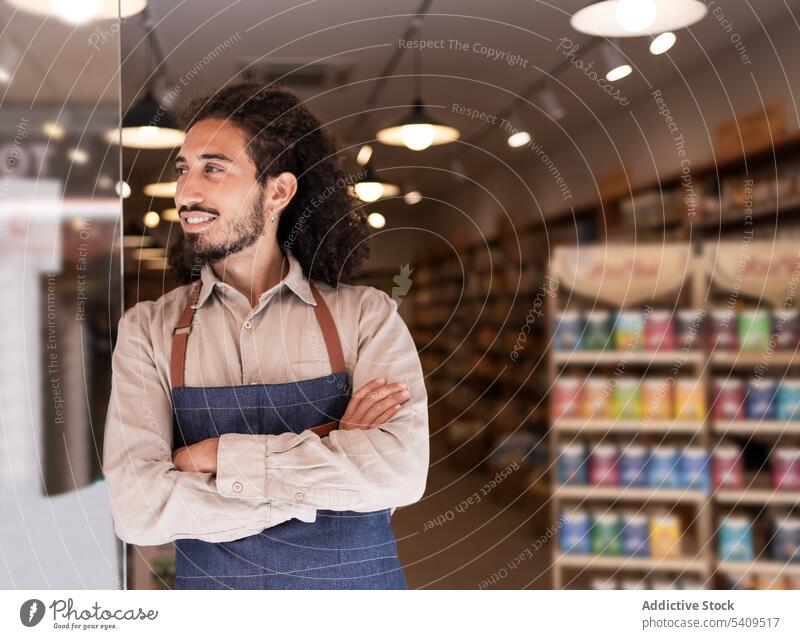 Cheerful man standing against lighted supermarket with goods smile confident portrait beard positive cheerful happy apron work friendly optimist uniform modern