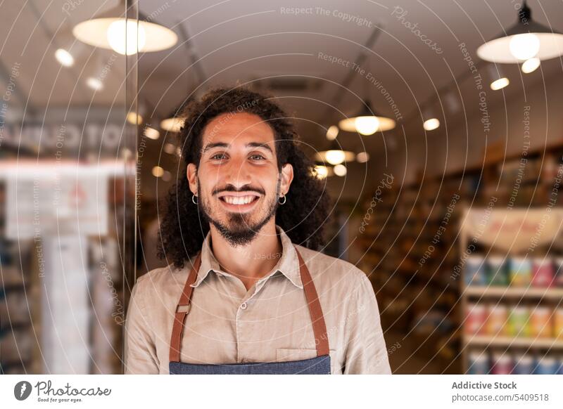 Cheerful man standing against lighted supermarket with goods smile confident portrait beard positive cheerful happy apron work friendly optimist uniform modern