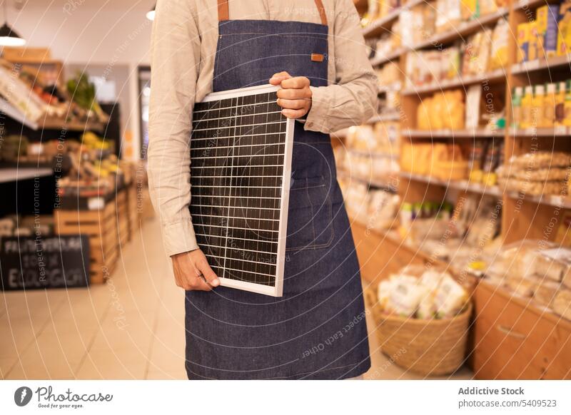 Anonymous crop seller holding portable solar panel in store man supermarket shop worker purchase modern device shopper energy generation male gadget alternative