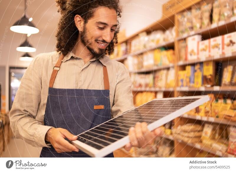 Cheerful ethnic seller holding portable solar panel in store man supermarket shop happy cheerful worker positive purchase modern device shopper energy smile