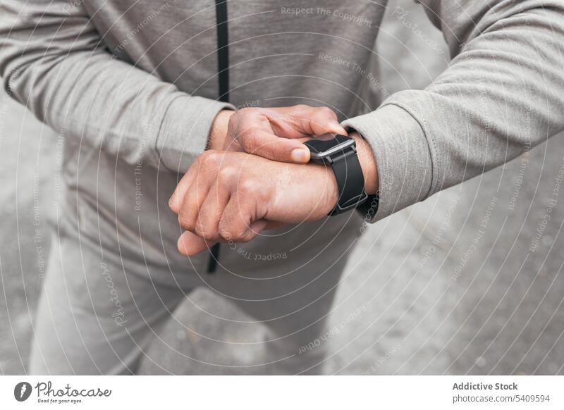 Unrecognizable man in sportswear standing and checking smart watch for time in daytime asphalt road athlete punctual schedule summer male fit guy outside