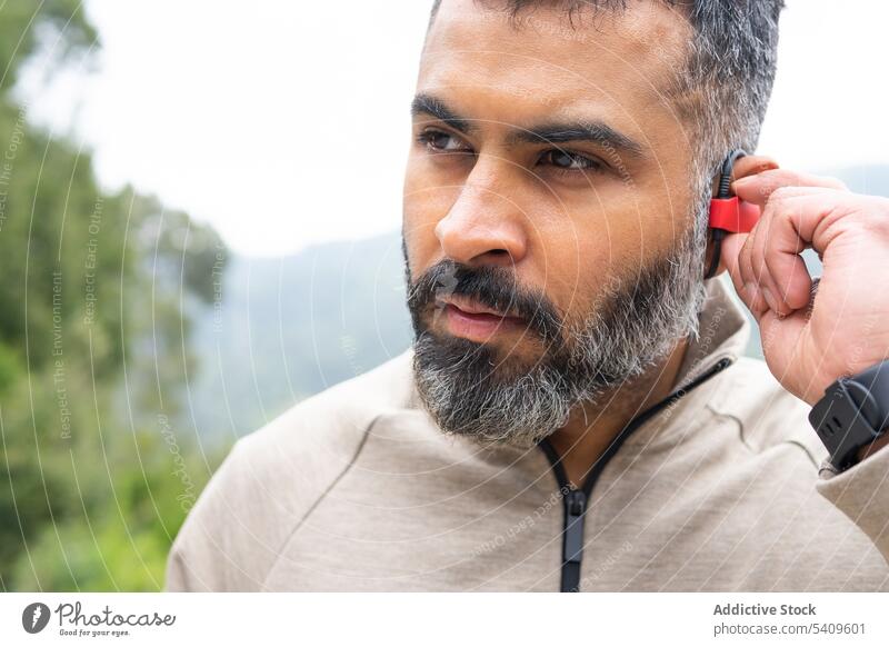Man in sportswear turning on a wireless earphone lifestyles vitality listen marathon wellbeing ethnicity jogger jogging listening runner innovation running