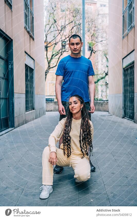 Stylish couple posing on street man woman city town building together outfit relationship wall braid style trendy sit hispanic pavement fashion daytime casual