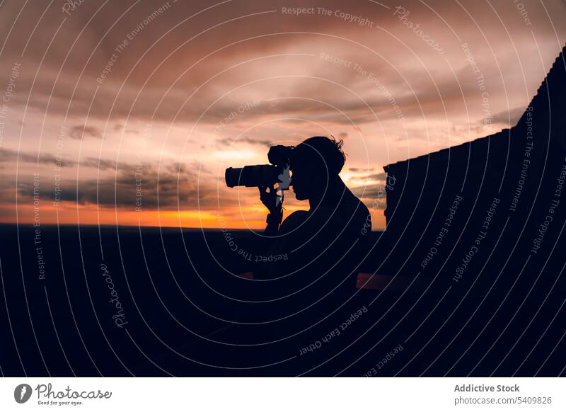 Unrecognizable man with camera taking picture of the evening orange sky with black clouds take photo sunset nature summer background male dark aim silhouette