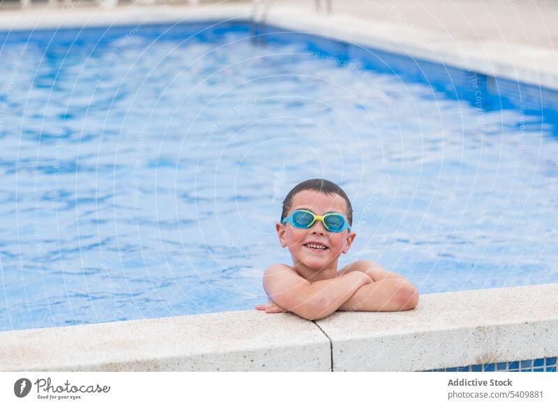 Happy kid in goggles at poolside standing in swimming pool in daylight child smile wet hair water enjoy glad hands crossed boy summertime vacation positive