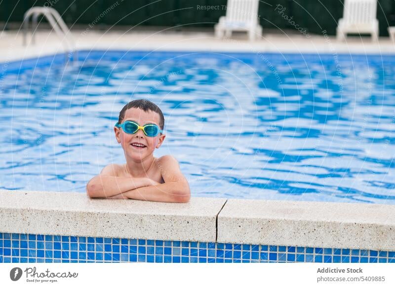 Happy kid in goggles at poolside standing in swimming pool in daylight child smile wet hair water enjoy glad hands crossed boy summertime vacation positive