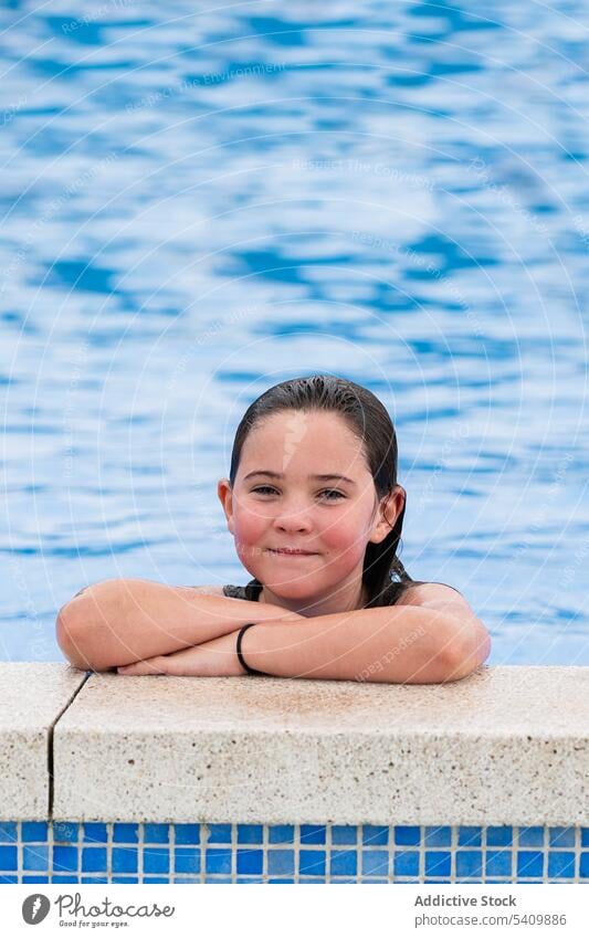 Happy kid at poolside standing in swimming pool in daylight child smile happy wet hair water enjoy glad hands crossed girl summertime vacation positive holiday