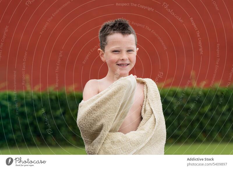 Happy kid standing in park with towel wrapped around body in daylight child portrait smile adorable happy glad cheerful friendly summer cute boy childhood