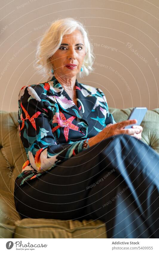 Senior woman sitting on sofa and using smartphone text message communicate comfort internet online at home female senior elderly cozy connection mobile gadget
