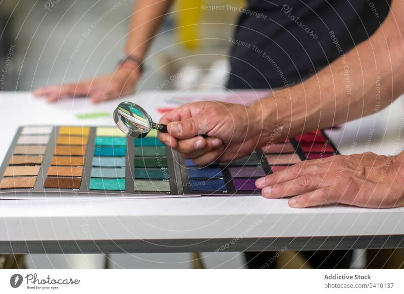Unrecognizable man using magnifier at desk to check fabric texture and quality person examine tool magnifying glass professional explore analyze workplace