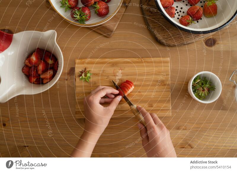 Anonymous person sliced strawberry in board over wooden table bowl knife fresh ripe vitamin delicious fruit jam natural organic healthy food tasty leaf sweet