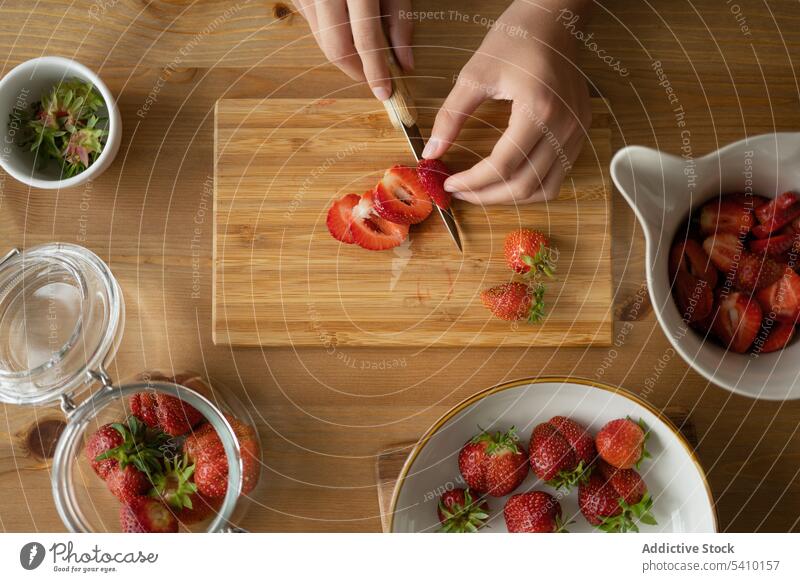 Anonymous person sliced strawberry in board over wooden table bowl knife fresh ripe vitamin delicious fruit jam natural organic healthy food tasty leaf sweet