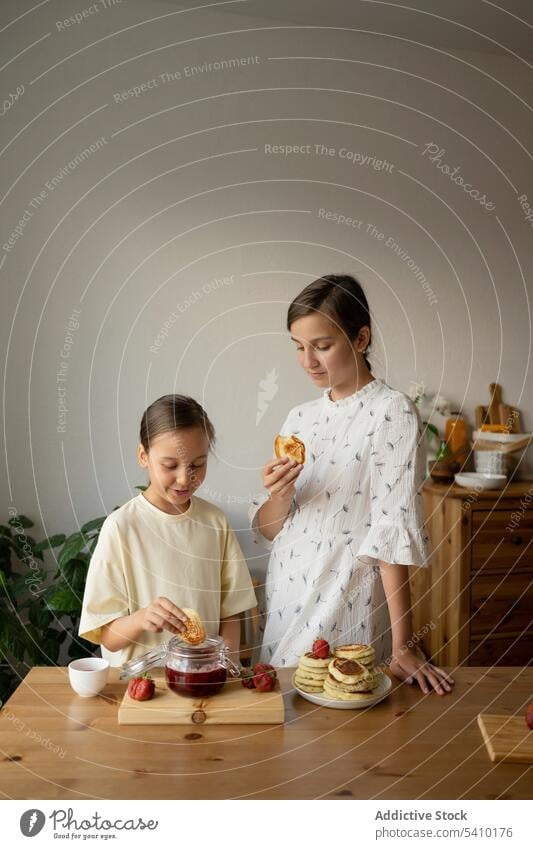 Positive sisters in having sweet breakfast girl strawberry eat kitchen food together pancake jam positive morning sibling family happy young child teen table