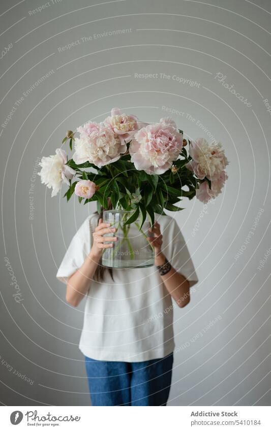 Unrecognizable preteen kid standing with blooming peony flowers in glass jar child fresh green leaf stem arrange floral blossom dress style vase daylight