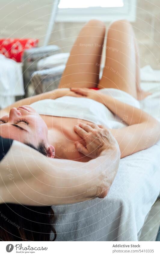 Young woman lying on bed during face massage therapy spa towel masseuse shoulder procedure wellness beauty relax sensual female young body masseur skin care