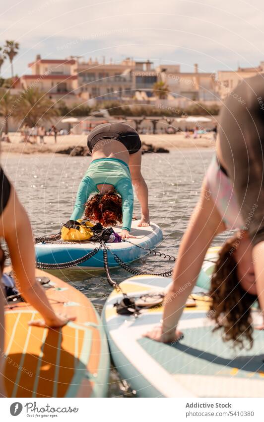 Young women in downward dog yoga pose on paddleboard woman practice exercise hobby wellness sea shore beach water healthy sup activity coast swimwear flexible