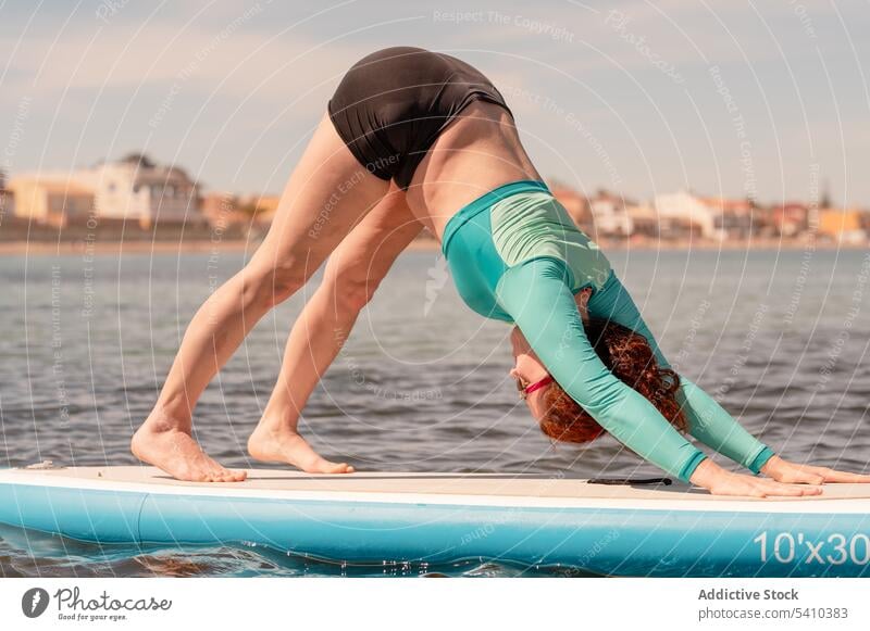 Woman doing yoga on paddleboard over sea woman practice stretch downward dog pose beach training seashore activity ocean flexible healthy water coast young